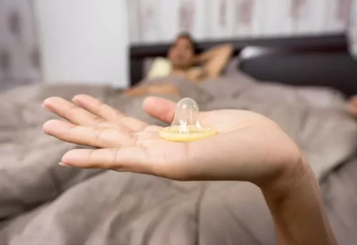 Kvinde står med kondom foran mand i seng