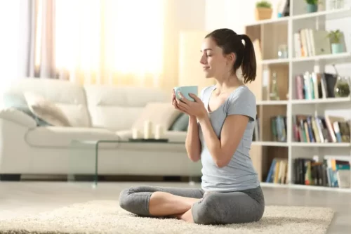 Kvinde mediterer med en kop te i hånden