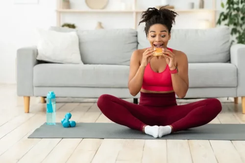 Kvinde spiser en burger efter træning som eksempel på fødevarer med højt glykæmisk indeks