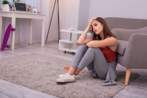 Ulykkelig ung kvinde sidder på gulv i soveværelset