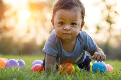 Baby kravler på græsplæne med bolde