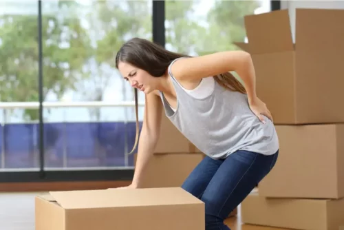 Kvinde oplever lændesmerter, da hun skal flytte en kasse