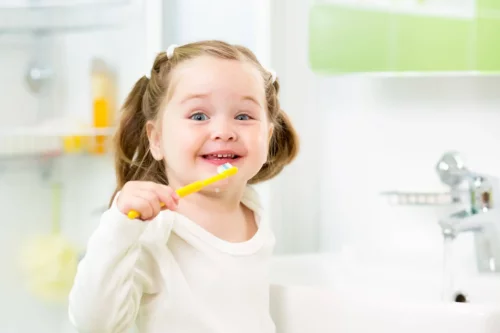 Pige børster tænder med gul tandbørste