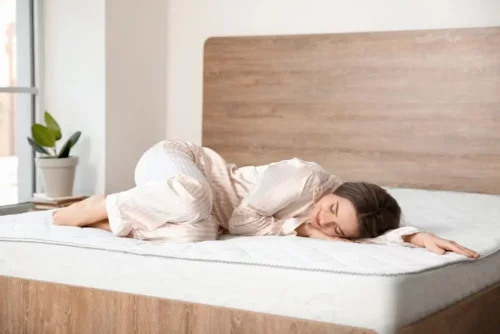 Kvinde ligger på seng uden sengetøj på