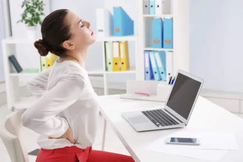 Kvinde ved skrivebord oplever rygsmerter