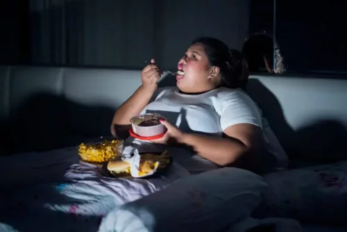 Overvægtig kvinde spiser i seng om natten