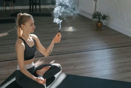 Kvinde på yogamåtte brænder røgelse og er ved at rense hjemmet med salvie