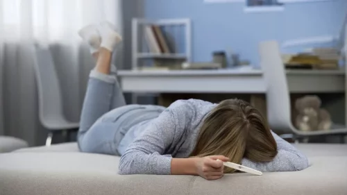 Frustreret kvinde ligger på seng med positiv graviditetstest