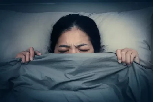 Kvinde gemmer sig under dyne, da hun er plaget af mareridt som søvnforstyrrelse