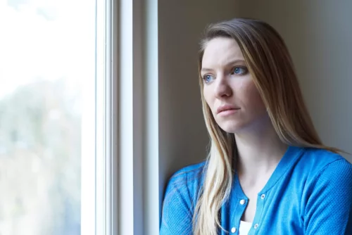 Bekymret kvinde ser ud af vindue og oplever følelsesmæssig undvigelse