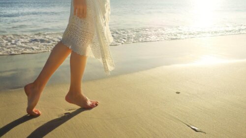 Kvinde går barfodet på strand